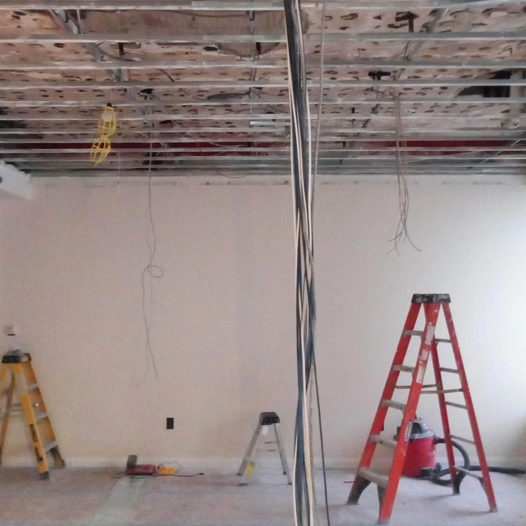 Gut-renovated New York City apartment interior with exposed ceiling joists, hanging wiring, and ladders during construction