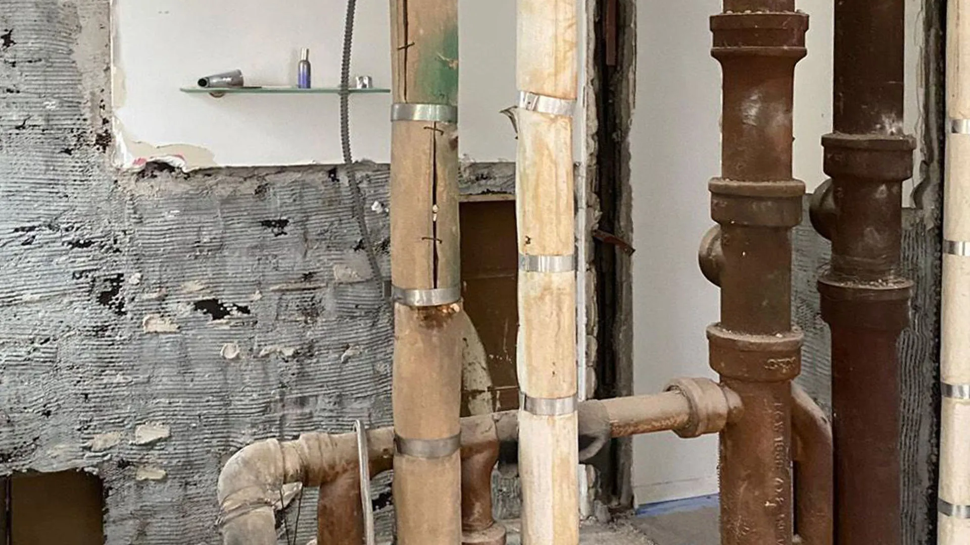 Exposed cast-iron pipes and stripped wall during an NYC apartment renovation