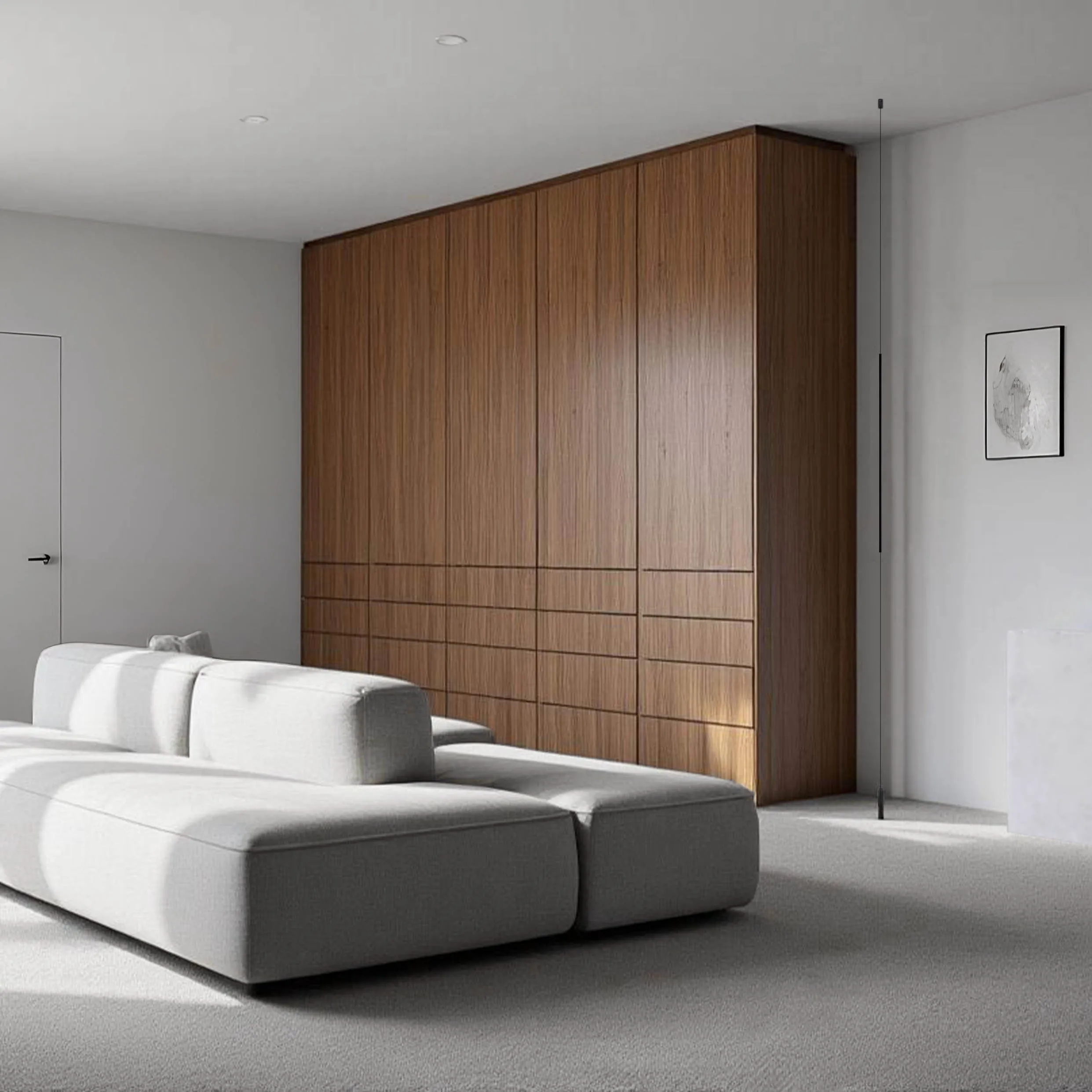 Full-height walnut millwork wall with recessed drawer fronts in a minimal NYC living room with a white modular sofa on grey carpet