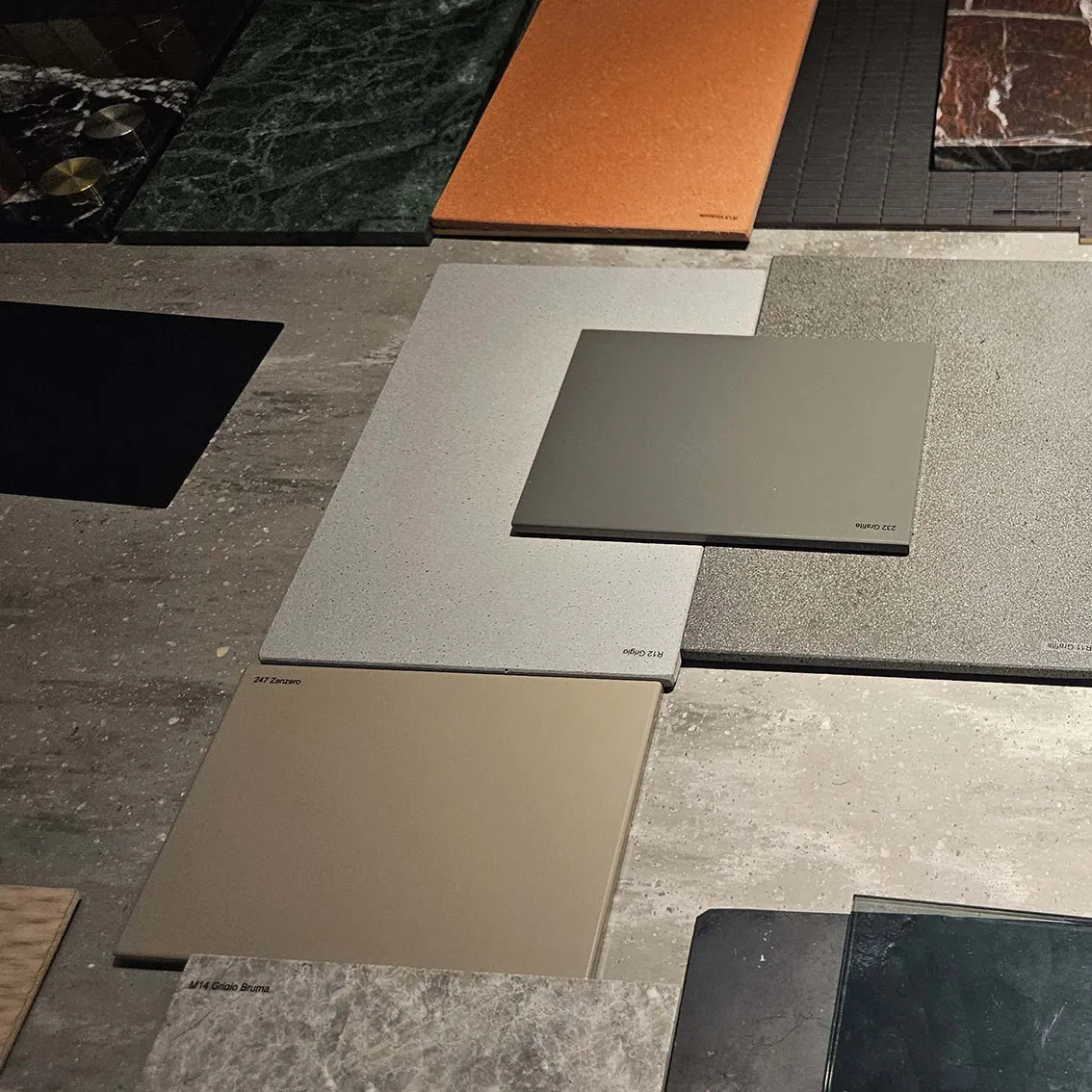 Labelled stone, tile and painted metal finish samples laid out on a concrete surface for an apartment renovation material selection