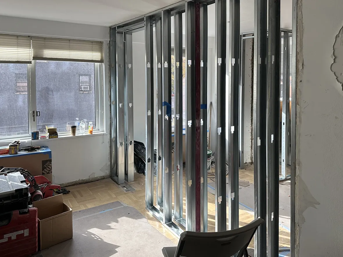 Kips Bay apartment during construction, with exposed wall framing, tools at left, and protective covering over parquet flooring.