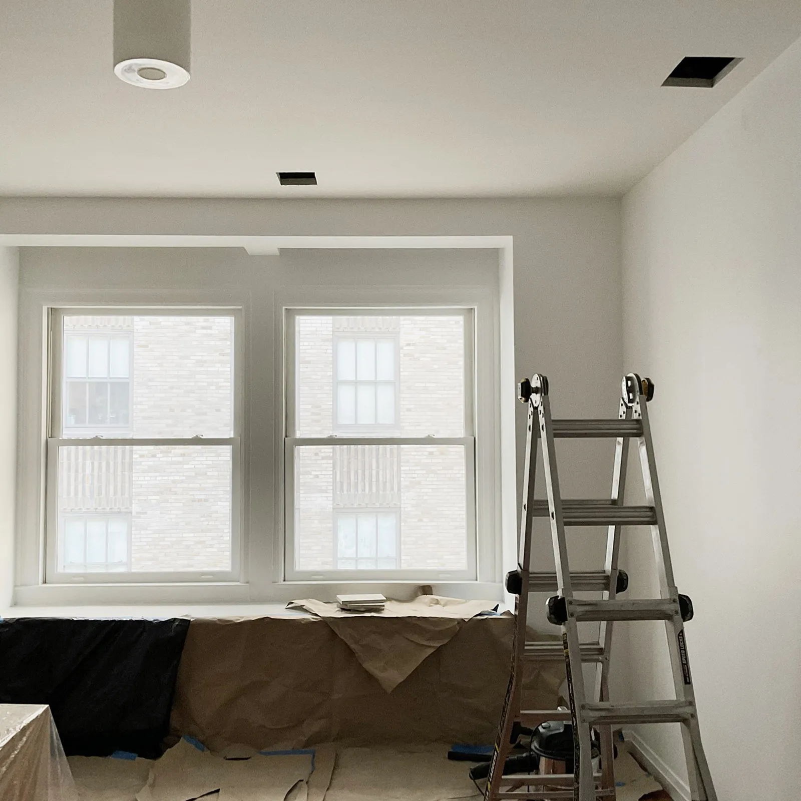 Interior construction at 55 Wall Street showing new room partitions, two windows overlooking Wall Street, and a ladder in the foreground.