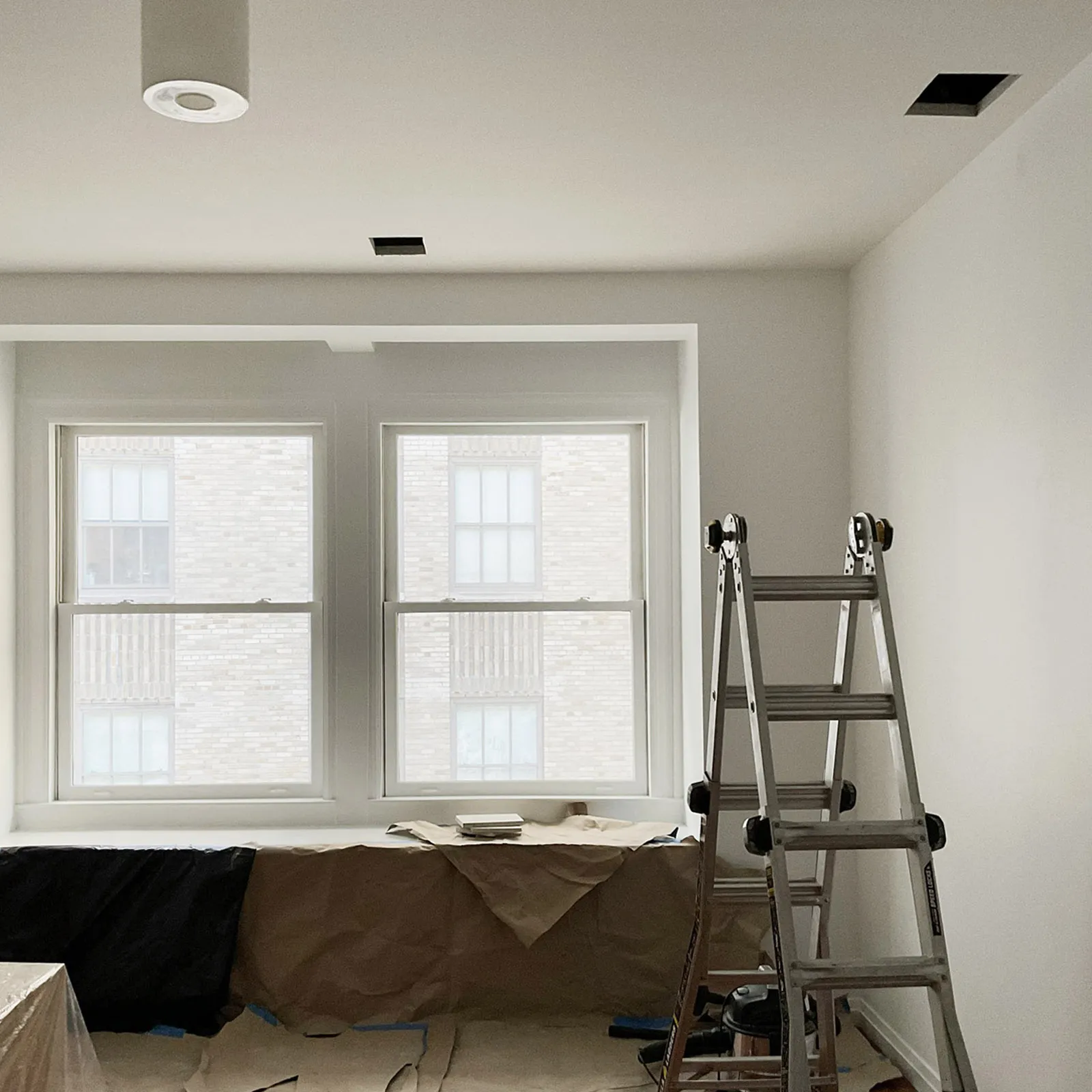 Newly installed and plastered walls at 55 Wall Street, with two rear windows, a ladder, and partial floor protection.