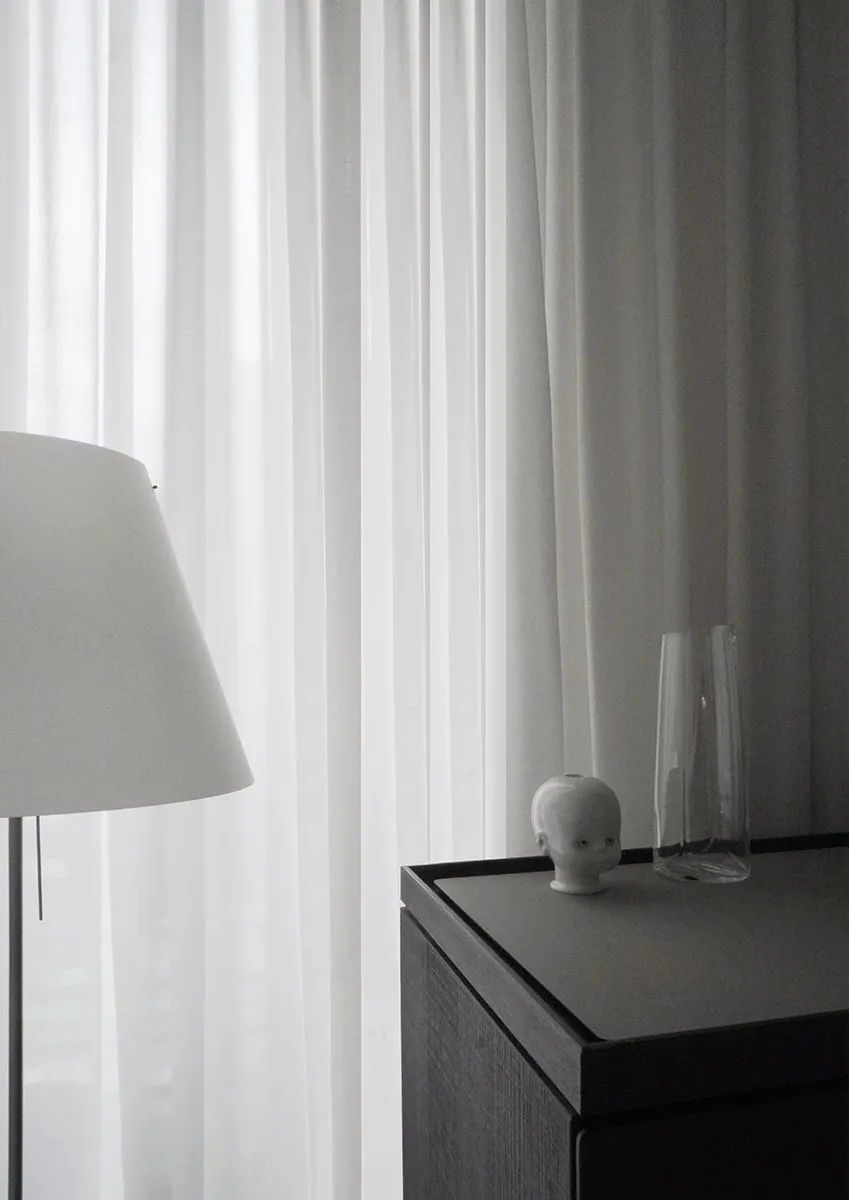 Brownstone interior design detail, a white floor lamp and small ceramic sculpture on a dark wood cabinet against sheer curtains