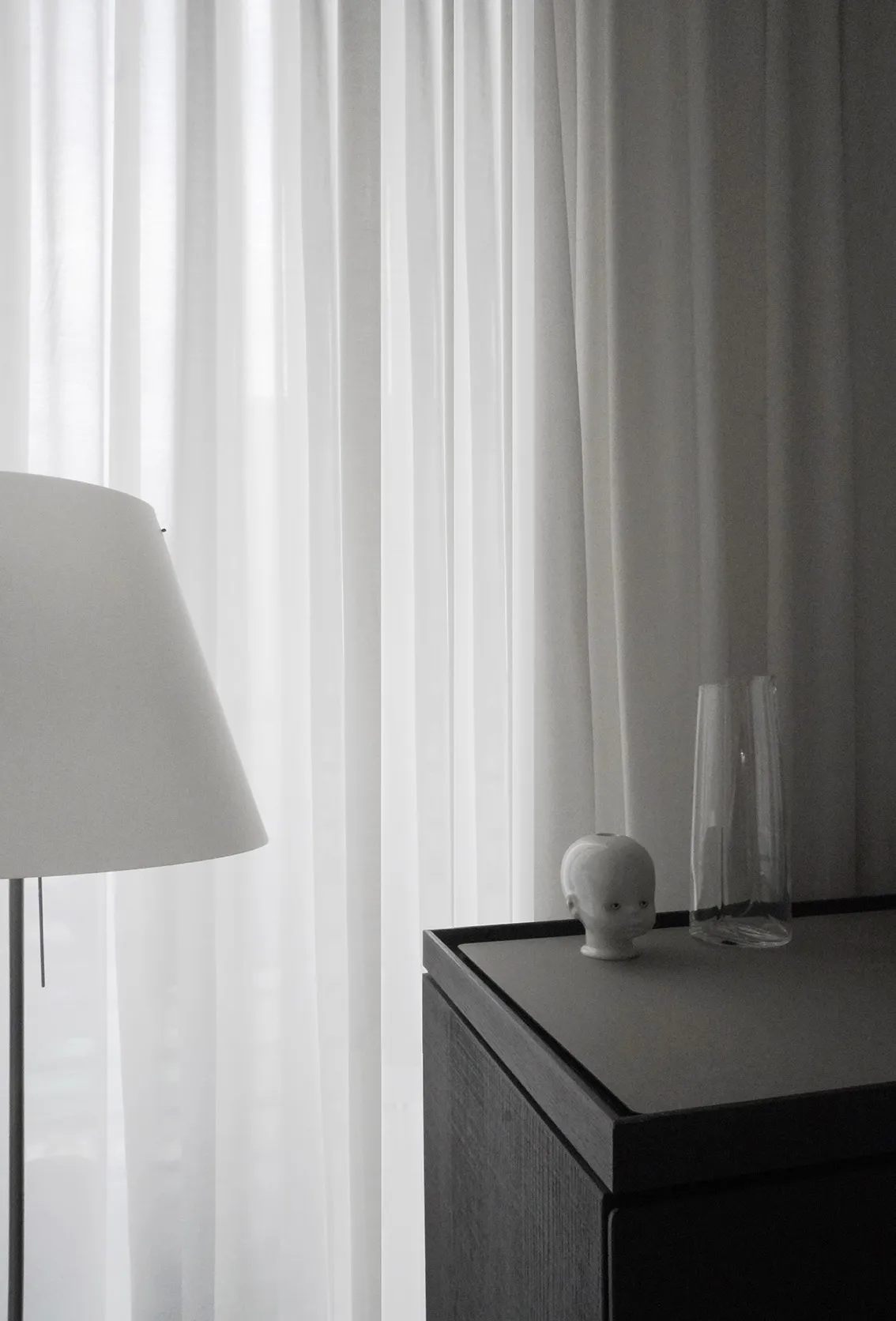 Modern minimal condo design showing Gray Ligne Roset console with a sculptural vase and porcelain head candleholder, beside a partially visible floor lamp and curtains.
