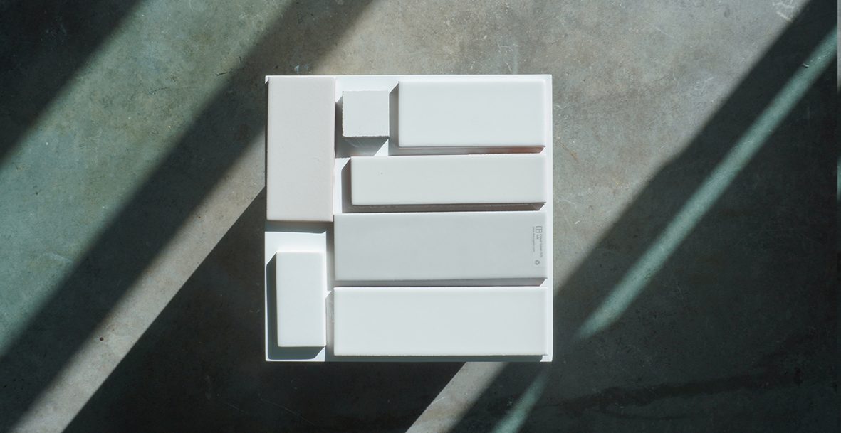 White architectural massing model on a dark surface in raking sunlight