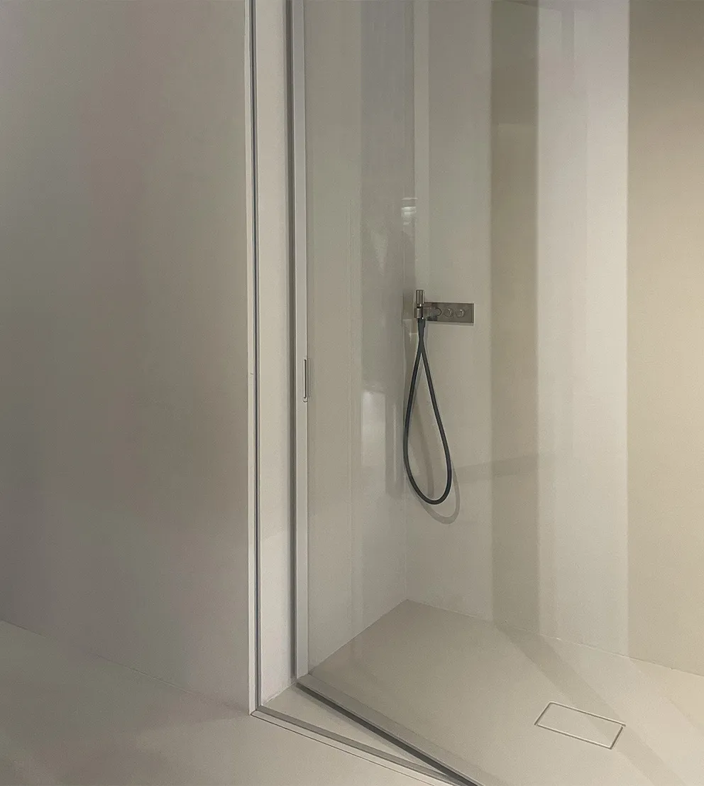 Modern bathroom design for NYC co-op showing neutral-toned shower with a partly open glass door, matching square drain cover, and minimal controls on the side wall.