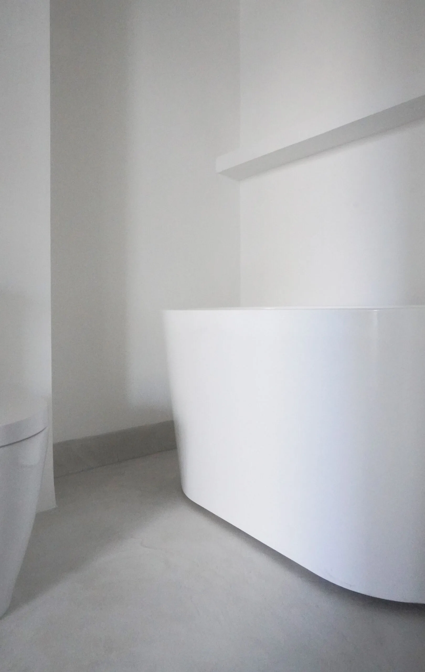 Modern minimal bathroom inspiration for NYC co-op with a freestanding bathtub, microcement flooring, a display shelf, and a Duravit toilet.
