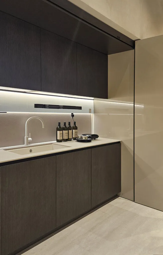 Contemporary prewar renovation design with ribbed dark ash-gray cabinets, white stone countertop, white enamel sink, and undercabinet lighting.