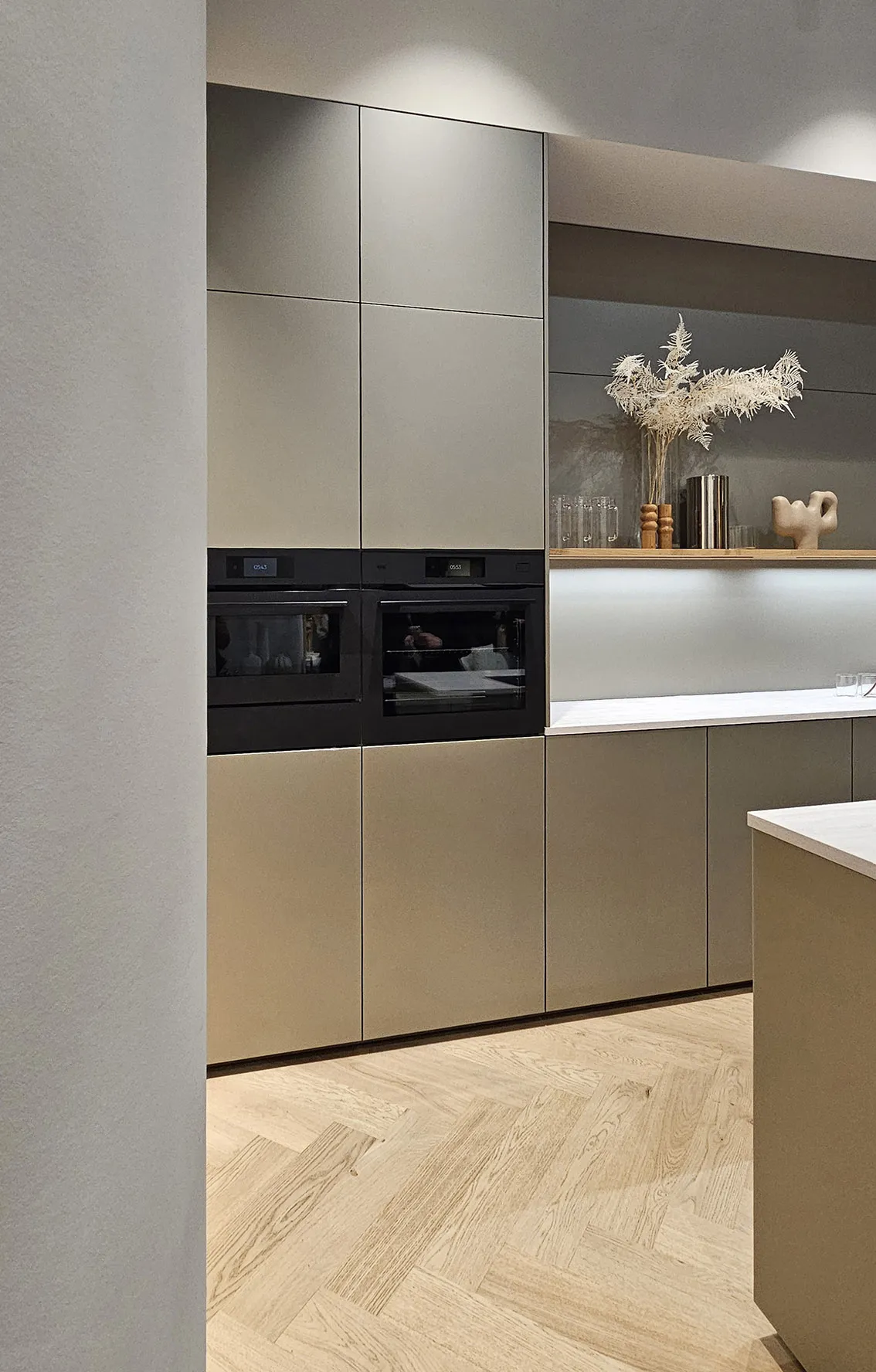 Prewar apartment kitchen with built-in wall oven and microwave, greige cabinets, and undercabinet lighting, shelf to right showing carefully curated architect chosen pieces.