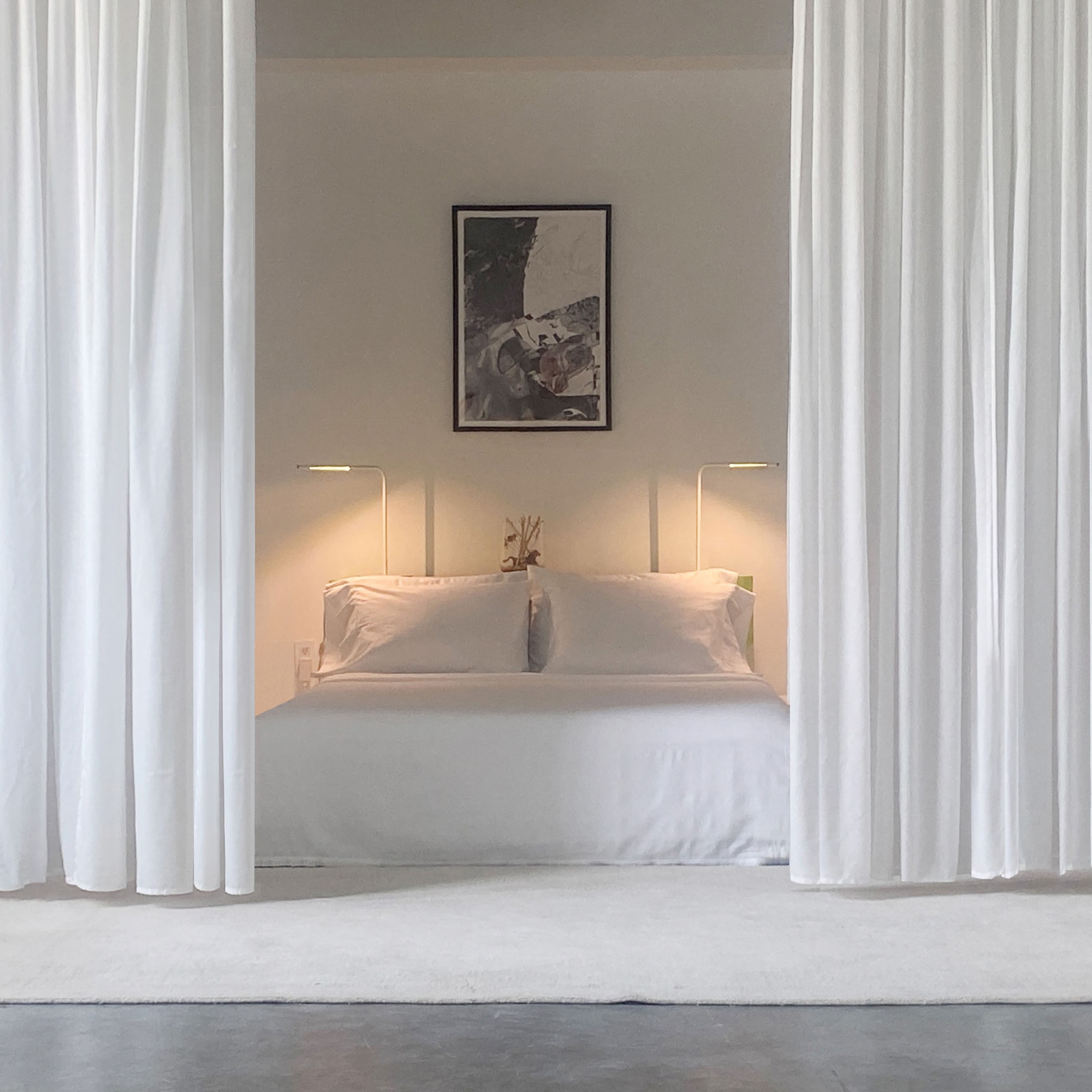 Bedroom in a NYC apartment remodeling project, a white bed framed by full-height sheer curtains with two wall-mounted reading lamps