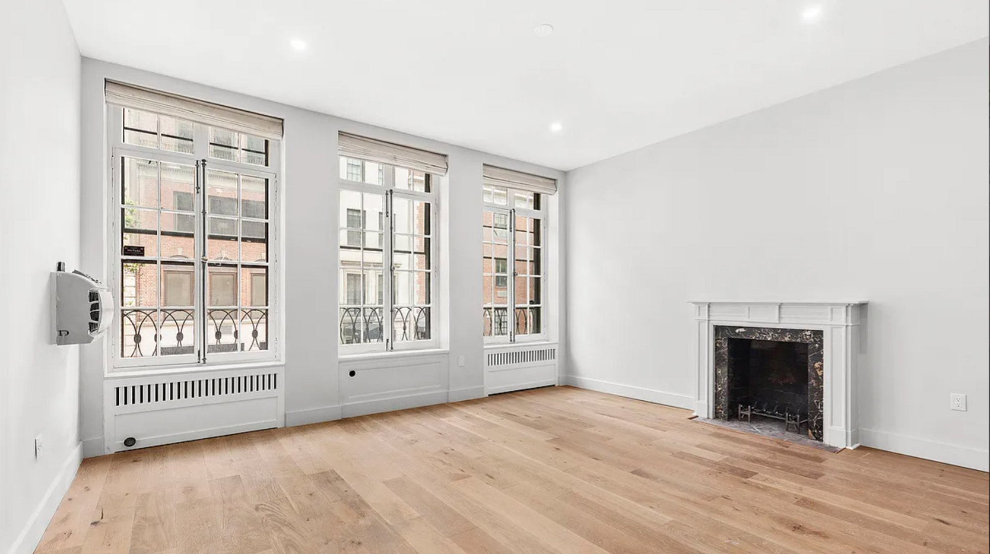 Existing condition of a 6-story Upper East Side townhouse before a gut renovation, an empty room with a marble fireplace and oak floors